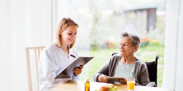Health visitor and a senior woman with tablet during home visit. A nurse making notes.